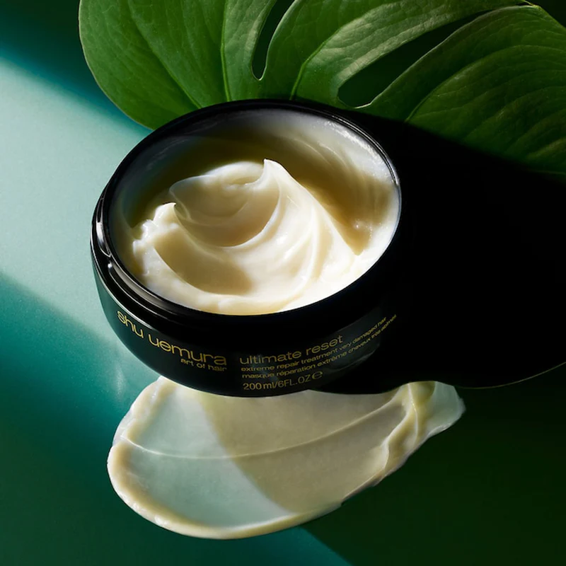 Un pot de masque Ultimate Reset de Shu Uemura sur une feuille de Monstera.