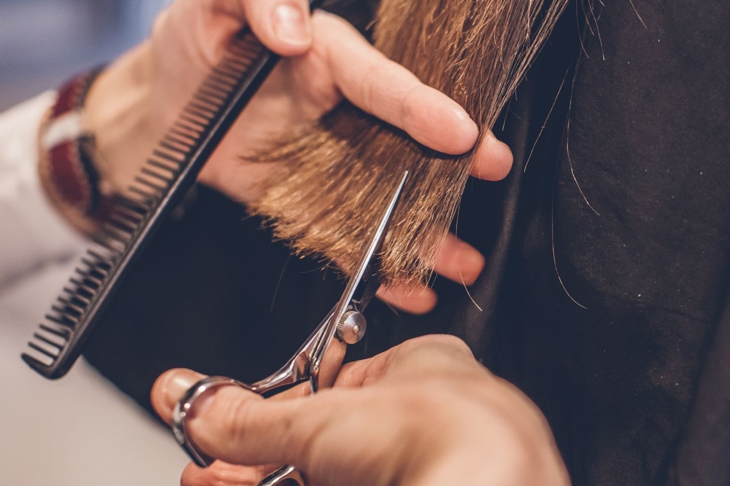 une main porte des ciseaux et coupe des cheveux pendant que l'autre main tient les cheveux et un peigne.