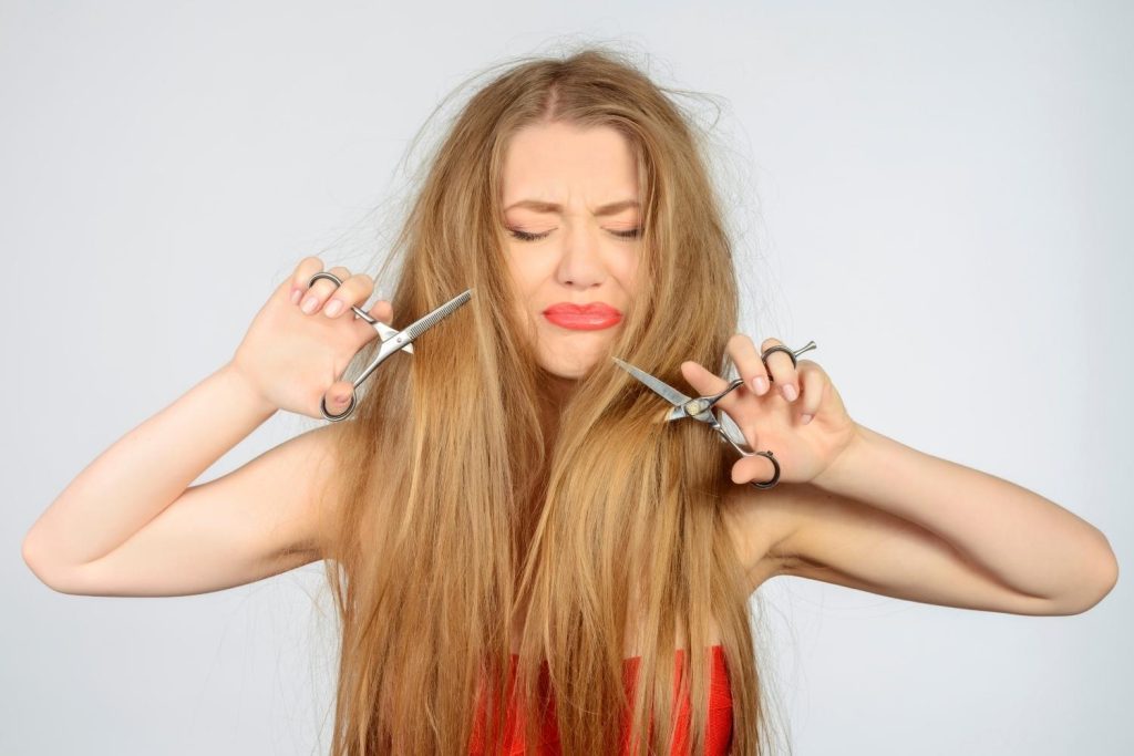 une femme aux cheveux longs se coupe elle-même les cheveux avec une paire de ciseaux dans chaque main.
