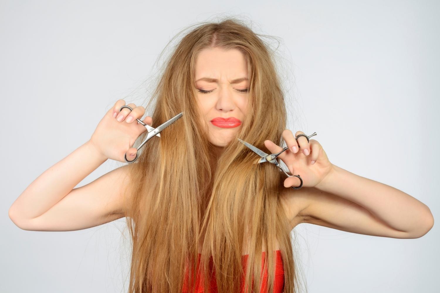 une femme aux cheveux longs se coupe elle-même les cheveux avec une paire de ciseaux dans chaque main.