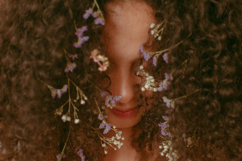 le visage d'une femme caché derrière des cheveux bouclés et ornés de fleurs d'automne.